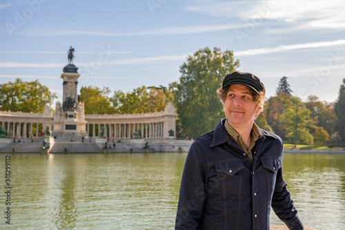 A father poses for a photo during a family trip to Madrid, in El Retiro park. He smiles contentedly and looks up at the distant scenery.
