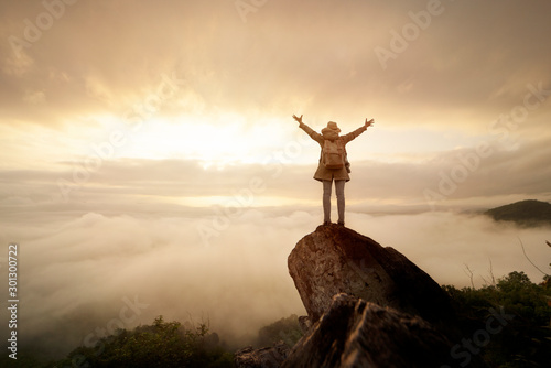 Backpacker woman raise hand up on top of mountain with sun sky and fog backgeound