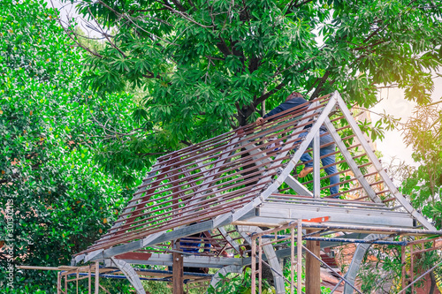 Welder and painter are helping to build a gable roof structure below a large mango tree.