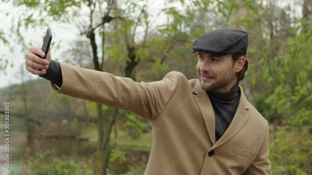 Cheerful business man taking selfie photo on his cell phone in the city park. Smiling person making mobile selfie. Handsome guy making self portrait on smartphone. Cheerful business man taking selfie photo on his cell phone in the city park. Smiling person making mobile selfie. Handsome guy making self portrait on smartphone.