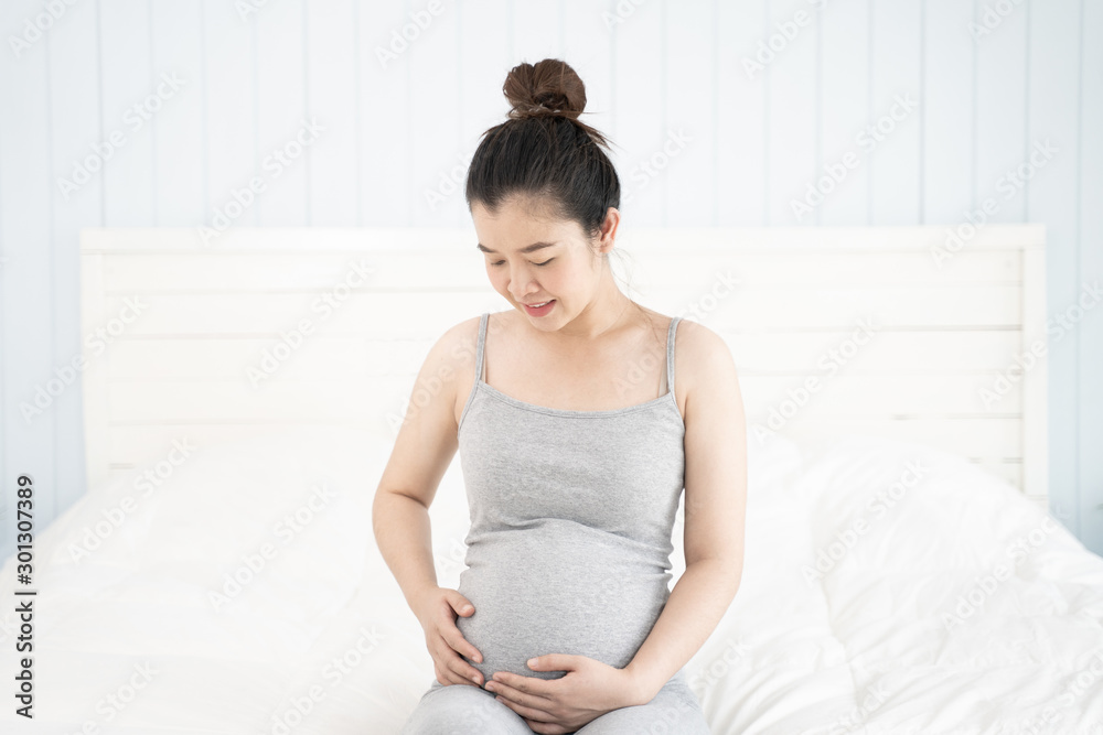 Pregnant woman sitting on the bed and touching her belly at home. Selective focus. Pregnant woman sitting on the bed and touching her belly at home. Selective focus.