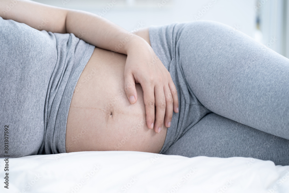Pregnant woman sleeping in bed at home. Close up of pregnant woman lying in bed and touching her belly. Pregnant woman sleeping in bed at home. Close up of pregnant woman lying in bed and touching her belly.