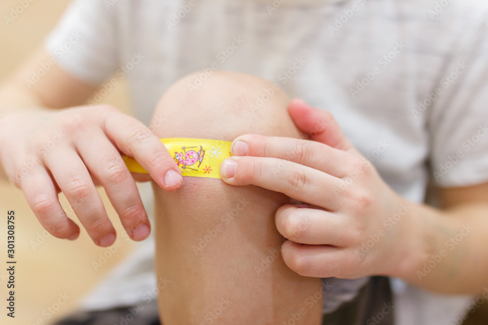 Naklejka premium Little boy with adhesive bandage on knee indoors, closeup