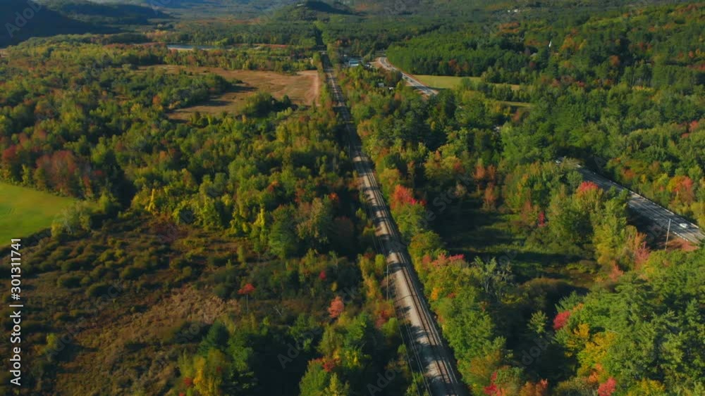 Aerial backward-reveal of a train track going through a green valley with mountains in the background on a clear day
