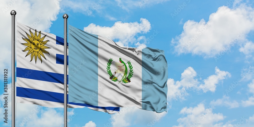 Uruguay and Guatemala flag waving in the wind against white cloudy blue sky together. Diplomacy concept, international relations. Uruguay and Guatemala flag waving in the wind against white cloudy blue sky together. Diplomacy concept, international relations.