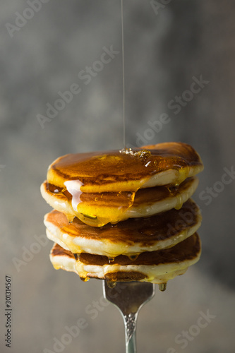 Tasty breakfast. Homemade stack pancakes on fork with honey or maple syrup on grey background.