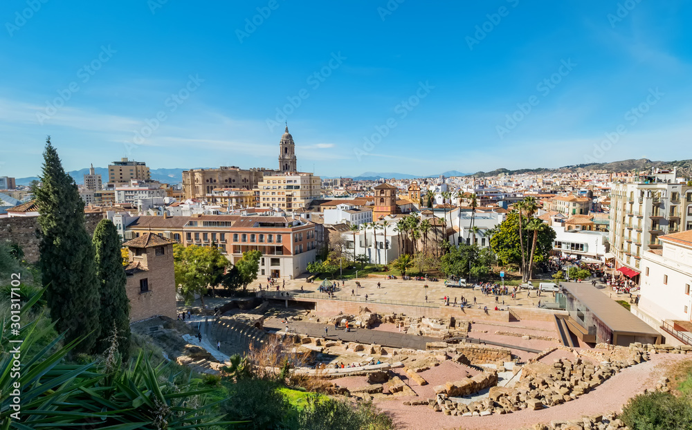 View of the roman theatre of Malaga, Spain on a sunny day. The Cathedral and Picasso Museum in the background.