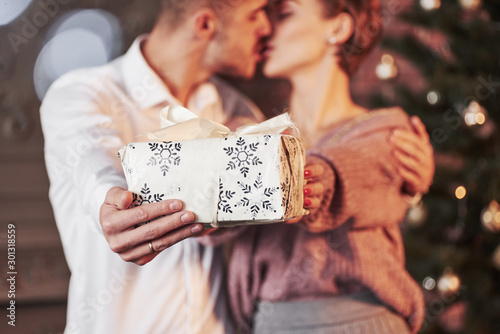 Kissing while holding gift box. Cute people. Nice couple celebrating new year in the new year decorated room