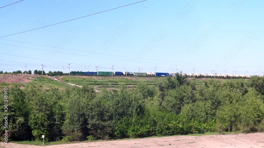 long freight train with building materials is moving by railway on the background of fields and forests in the summer on a sunny day. long freight train with building materials is moving by railway on the background of fields and forests in the summer on a sunny day.
