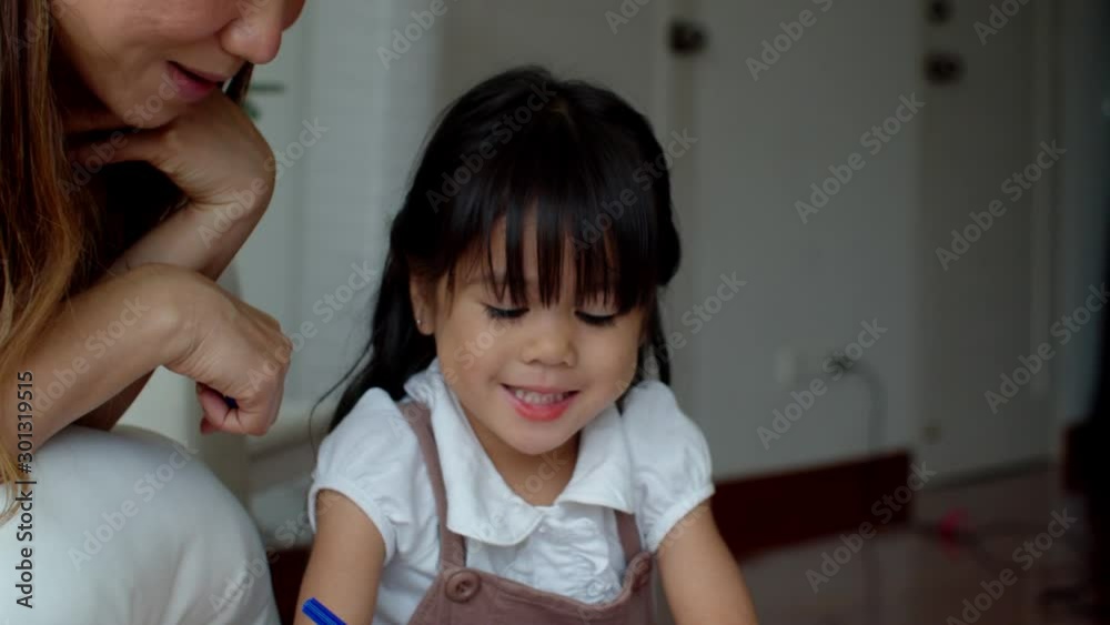 Young mother looking her daughter paint colour on paper