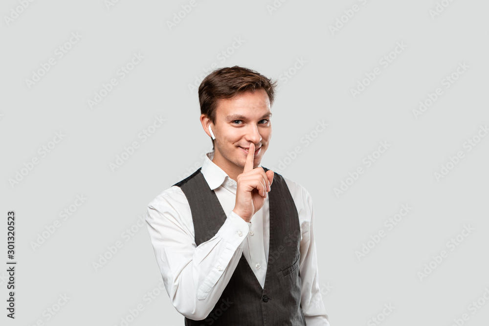 Young handsome man in a white shirt and grey vest holding finger close to mouth hand close to chin. Young handsome man in a white shirt and grey vest holding finger close to mouth hand close to chin.