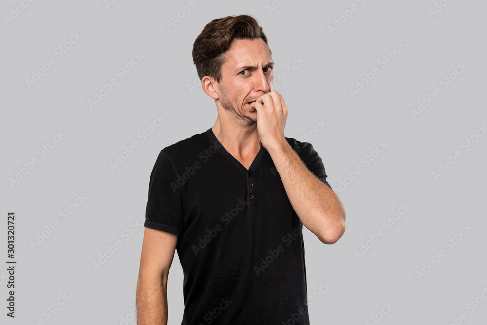 Man in a black tee shirt biting his nails feeling anxious isolated over grey background. Man in a black tee shirt biting his nails feeling anxious isolated over grey background.