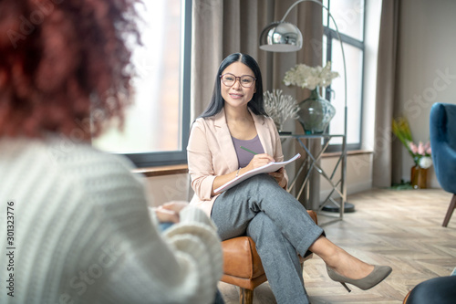 Pleasant psychologist wearing grey trousers smiling to client photo