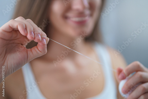 Happy healthy woman uses dental floss for brushing teeth and oral hygiene at home. Teeth oral care