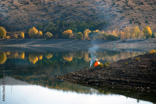 Camping in autumn forest, reflection and red tent on the lake.