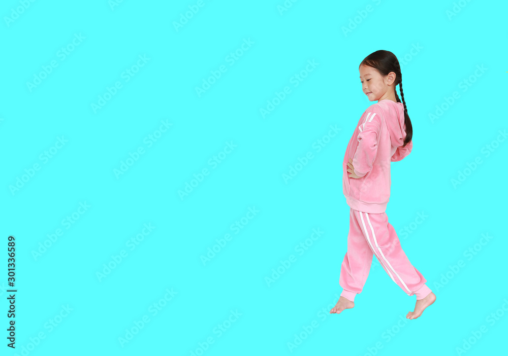 Portrait of little Asian child girl in pink tracksuit or sport cloth sitting and doing exercises isolated over cyan background with copy space.