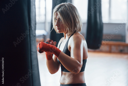 Workout strokes. Female boxer is punching the bag. Blonde have exercise in the gym © standret