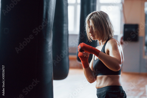 That girl can beat some people. Female boxer is punching the bag. Blonde have exercise in the gym © standret