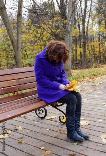 Lonely girl in the park on a bench with autumn leaves in her hands. © svdolgov