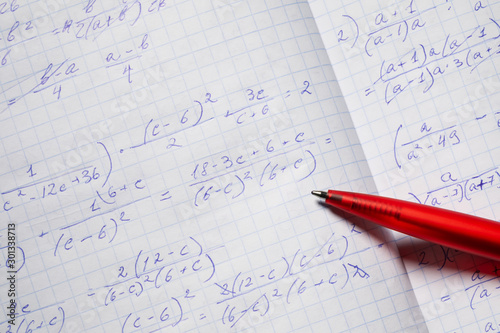 Algebraic calculations in open graph notebook with red pen. White graph paper with math fractions