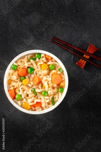 Ramen cup, instant noodles in a plastic cup, shot from above with chopsticks and copy space on a dark black background
