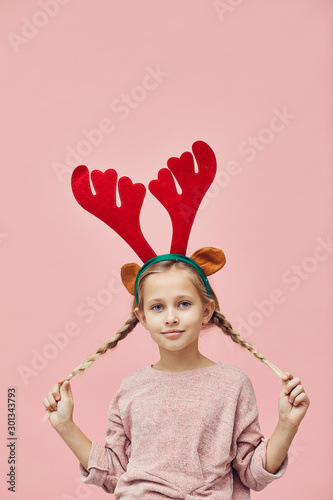 Portrait of pretty little girl in deer antlers posing at camera over pink background