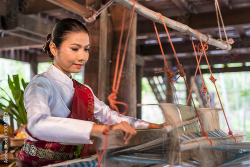 Asian female weaving silk sari on loom.young woman works on cotton or silk weaving with traditional hand weaving loom.Asian traditional culture. concept of life, people,  Small business,Southeast Asia © Joke Phatrapong