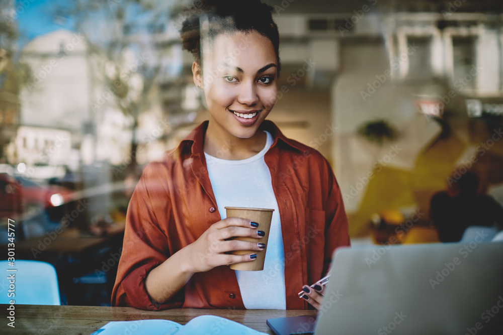 Portrait of cheerful female freelancer sitting at table with modern laptop computer and smiling at camera during distance job in coworking space, happy woman enjoying coffee break from remote work Portrait of cheerful female freelancer sitting at table with modern laptop computer and smiling at camera during distance job in coworking space, happy woman enjoying coffee break from remote work