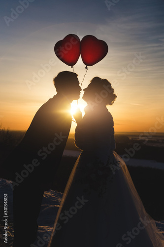 the light of the sunset through the kissing silhouettes of the newlyweds with red balls in the form of hearts