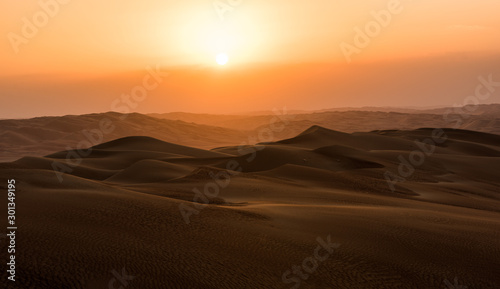 sunset in the desert, on the horizon you can see the orange sun setting behind the dunes far away