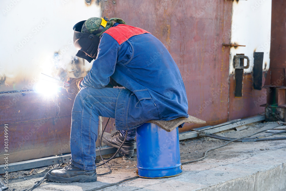 Welder at work. Welding steel sheets of the shell of the reservoir for filling with gasoline and petroleum products in the tank park at the refinery.