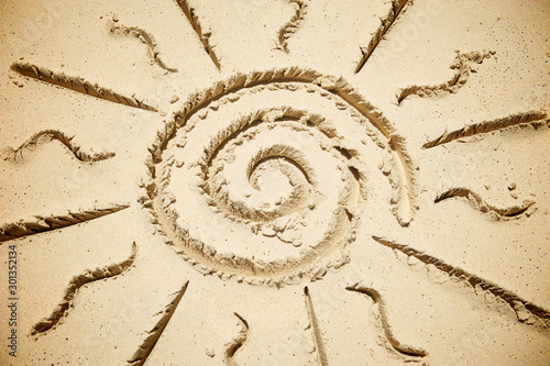 Stylised spiral sun with rays drawn on a in smooth sand on a sunny beach