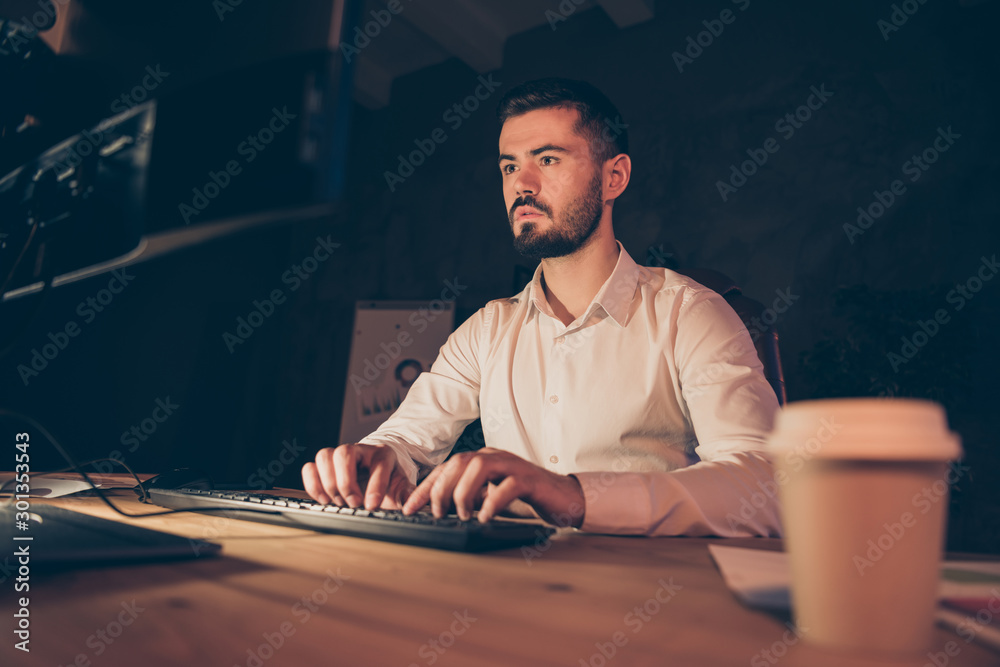 Portrait of concentrated businessman sit table desk work on computer pc stay in evening at dark office want finish project to his boss in loft Portrait of concentrated businessman sit table desk work on computer pc stay in evening at dark office want finish project to his boss in loft