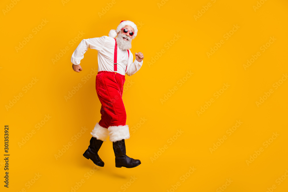 Full size profile side photo of funky crazy grey hair beard grandfather in red santa claus hat jump go run x-mas eve discounts isolated over yellow color background Full size profile side photo of funky crazy grey hair beard grandfather in red santa claus hat jump go run x-mas eve discounts isolated over yellow color background
