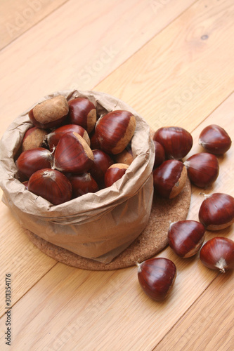 Bunch of ripe chestnuts in a paper bag on wooden background on selective focus