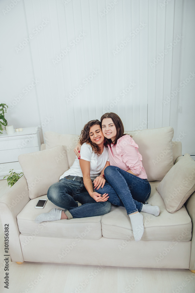 Two amazing girls sitting on the sofa, hugging one another, smiling lovely, looking at the camera. Two amazing girls sitting on the sofa, hugging one another, smiling lovely, looking at the camera.