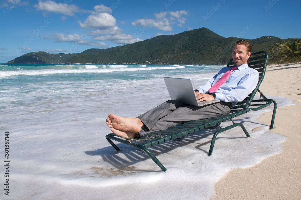 Businessman typing on his laptop on a beach chair working remotely from the shore of an empty tropical beach
