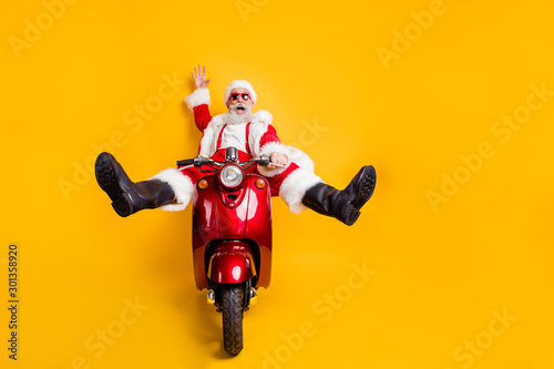Full size photo of amazed funny crazy santa claus in red hat drive fast scooter want hurry on x-mas christmas party shirt suspenders isolated over yellow color background