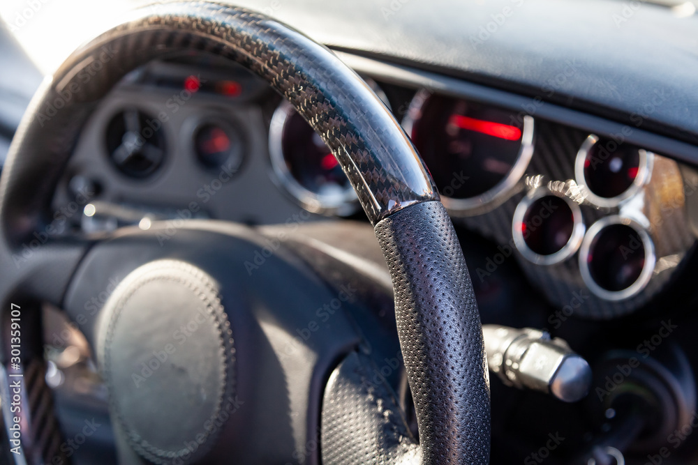 Carbon steering wheel of a black car in the workshop tightened and perforated with natural leather close up