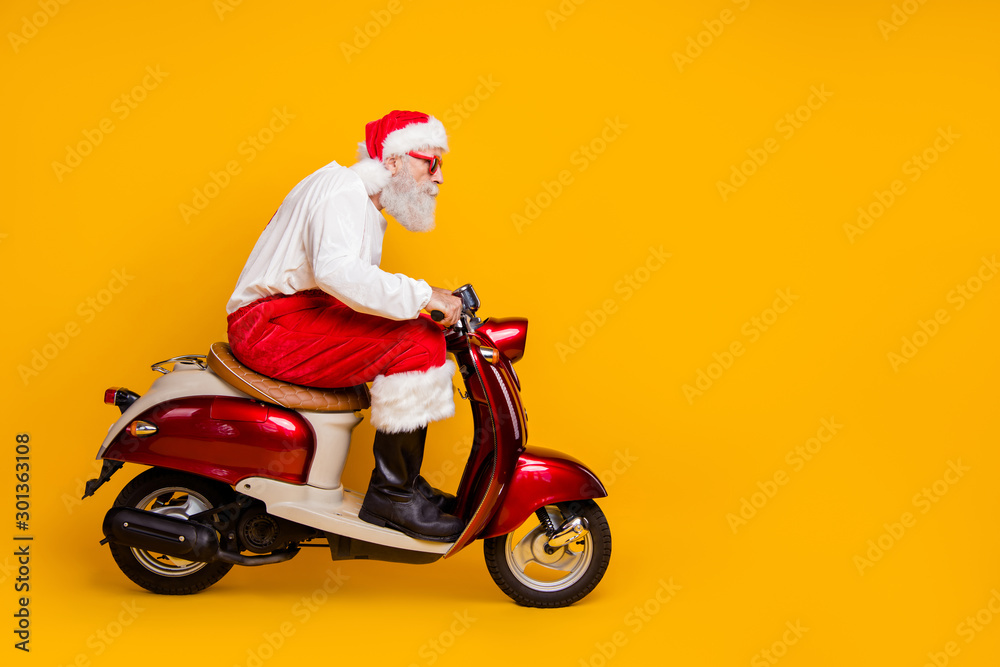 Full body profile photo of santa white hair grandpa riding speed x-mas theme party by bike wear trendy sun specs trousers cap shirt boots isolated yellow color background