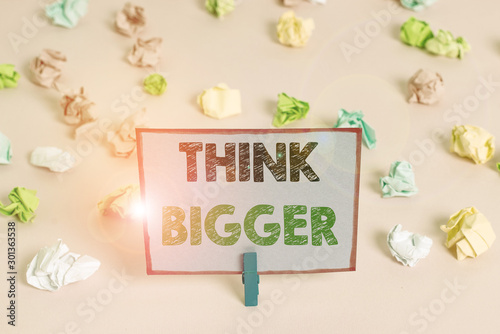 Writing note showing Think Bigger. Business concept for being able to dream and visualise what you can achieve Colored crumpled papers empty reminder pink floor background clothespin © Artur