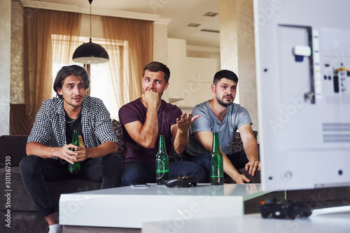 It's a defeat. Sad three friends watching soccer on TV at home together photo