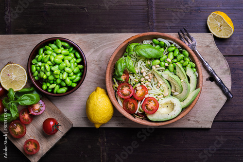 A fresh healthy salad with zoodles zucchini noodles, cherry tomatoes, avocado and edamame beans on a dark background