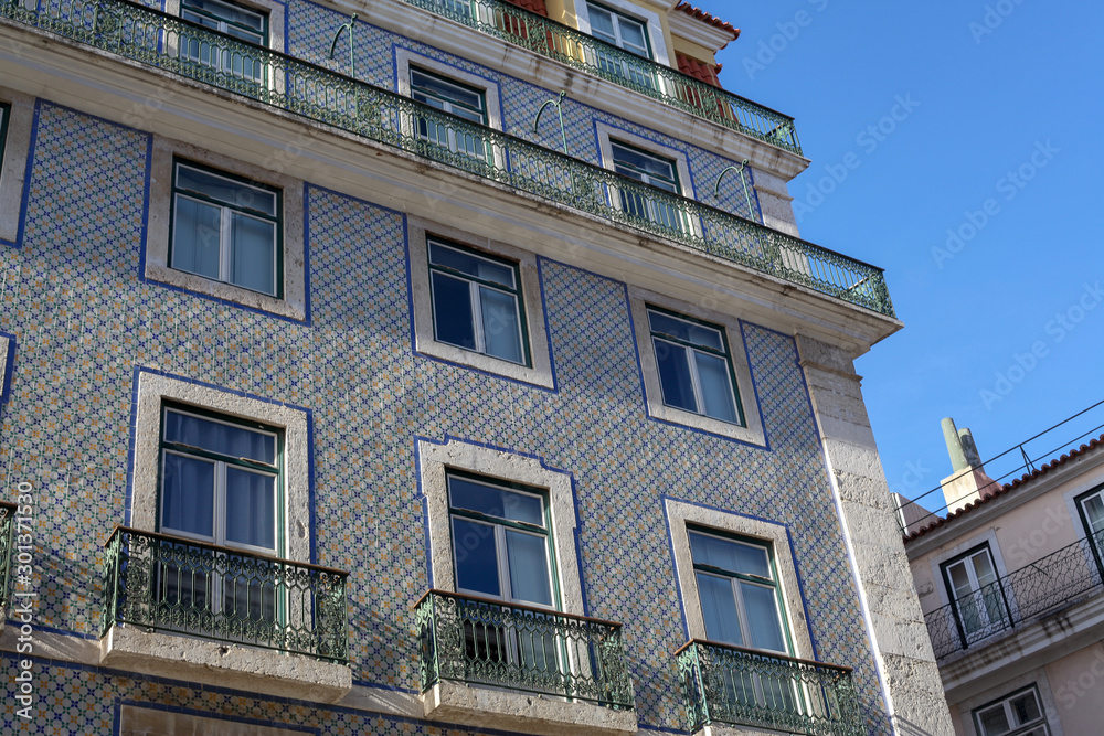 Naklejka premium A beautiful architecture of the traditional tiled walled facade with large glass doors and windows and the iron balcony in the city of Lisbon in Portugal