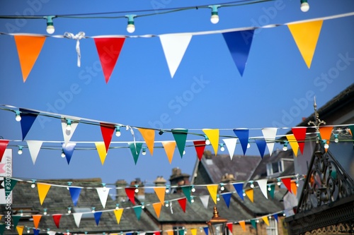 Bright colorful bunting or pennant flags hanging across pretty village street against blue sky for a traditional celebration, multi coloured.