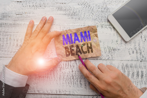 Conceptual hand writing showing Miami Beach. Concept meaning the coastal resort city in MiamiDade County of Florida Hand hold note paper near writing equipment and smartphone photo
