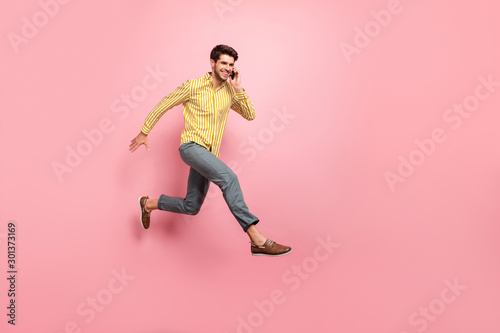 Full body profile photo of handsome guy jump high hold telephone speaking with girlfriend rushing date wear striped shirt pants isolated pink color background