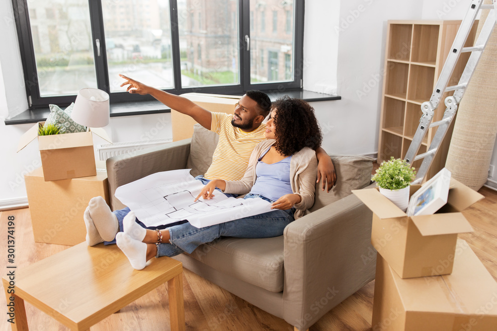 mortgage, people and real estate concept - happy african american couple with boxes and blueprint moving to new home mortgage, people and real estate concept - happy african american couple with boxes and blueprint moving to new home