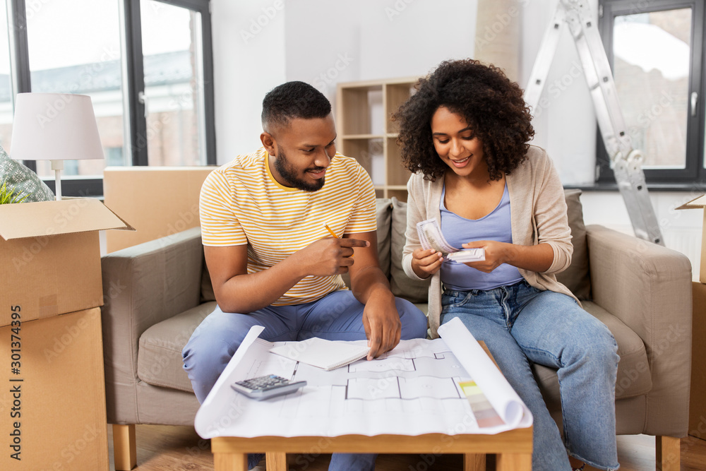 Fototapeta premium mortgage, moving and real estate concept - happy african american couple with blueprint and calculator counting money for repair costs to new home