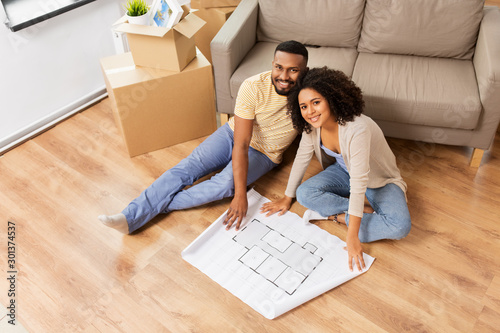 mortgage, people and real estate concept - happy african american couple with boxes and blueprint moving to new home photo